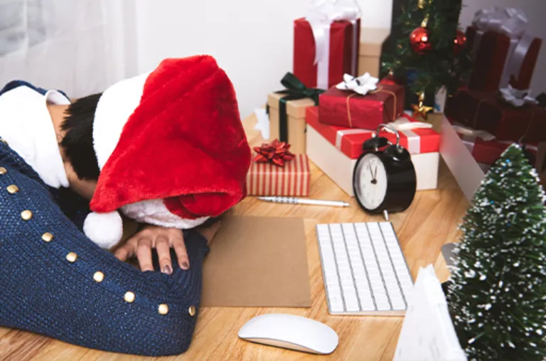 A person wearing a santa hat laying their head down on a desk.