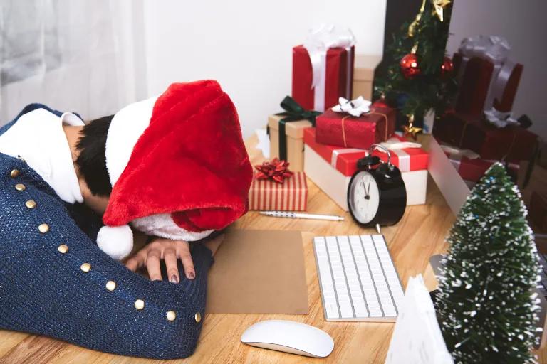 A person wearing a santa hat laying their head down on a desk.