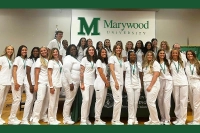 A group of nursing graduates from the Class of 2024 is pictured in nursing whites with a Marywood University banner behind them. Marywood Nursing Graduates Achieve Perfect 100% Pass Rate on National Exam