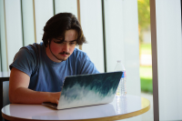 man sitting at table near window with laptop and water bottle