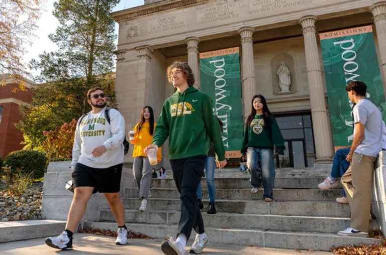 Various students walking down the stone steps in front of  the Liberal Arts Center building with Roman columns and Marywood banners.