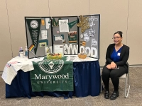 A Marywood Social Work student sitting next to a display table. The School of Social Work Holds Fall 2024 Symposium