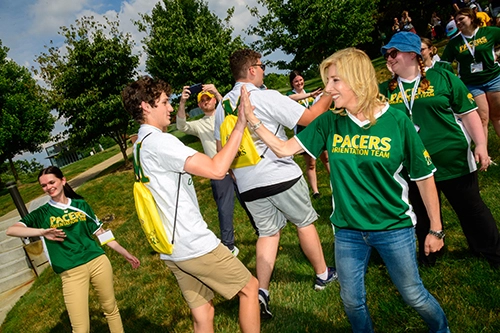 people in green shirts that say PACERS highfiving students in white shirts with M on the back wearing yellow sling bags