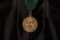 A gold engraved Marywood commencement medal on a green ribbon against a black graduation robe Class of 2025 Commencement Medalists